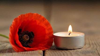 Burning candle next to a red poppy flower on a wooden table with a solemn and reflective mood for Remembrance Day tribute with copy space
