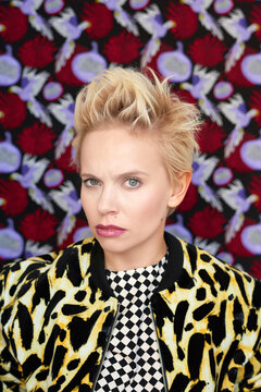 Expressive fashion model. Portrait of young trendy Caucasian woman with short blond hair frowning at camera on patterned background