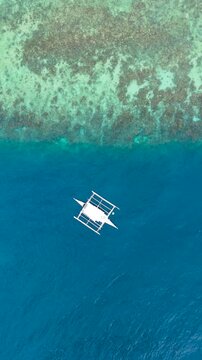 Aerial white outrigger boat floats on clear blue ocean water, with coral reefs in shallow turquoise areas, Palau.