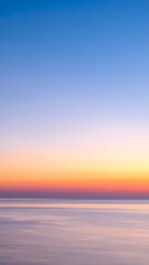 Obraz premium ​A serene seascape at twilight. The sky displays a stunning gradient from deep blue to warm orange over a calm, reflective ocean, creating a peaceful, minimalist scene.