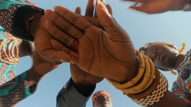 From below view of three young Black people in ethnic clothes joining their hands, symbolizing unity and solidarity