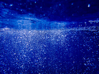 Fototapeta premium Underwater photography of the deep ocean with the ocean surface rippled with bokeh, bubbles, and lens flare great for water background with room for copy, Sunlight underwater with air bubbles rising.