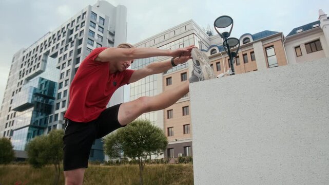 Low angle shot of adult Caucasian athlete doing hamstring stretch exercise outside in city