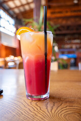 Refreshing tropical cocktail, layered red and orange drink in tall glass on wooden table