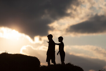 Two boys play on hay bales at sunset with a dramatic sky in the background, creating a serene rural atmosphere © Светлана Лазаренко