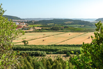Drone view of a golden rural field with hay bales at sunset in Óbidos, Portugal, showing warm light, agricultural landscape and peaceful countryside atmosphere.