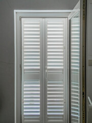 Interior view of closed white shutters with louvered panels softly filtering daylight, providing modern privacy, quiet, and geometric pattern to a peaceful home environment.