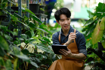 Young Asian man studies greenhouse plants with technology and observation