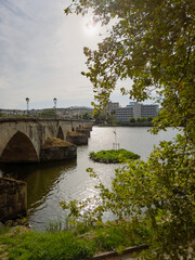 Mirandela, Portugal: The iconic pedestrian bridge over the Tua River, framed by lush trees and cityscape, offers a scenic route connecting nature and urban charm in this historic town.