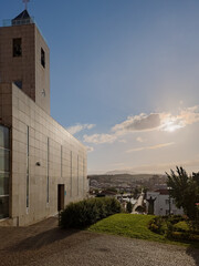 Partial view of the modern church tower and facade in Mirandela, Portugal, with a panoramic cityscape and sunset sky, capturing local faith, architecture, and urban life in a tranquil evening scene.