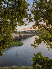 Mirandela, Portugal: The iconic pedestrian bridge over the Tua River, framed by lush trees and cityscape, offers a scenic route connecting nature and urban charm in this historic town.