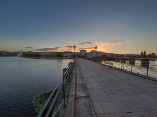 Pedestrian bridge over the Tua River in Mirandela, Portugal, leads to the city center at sunset. Evening light, calm water, and urban skyline create a tranquil and scenic connection.