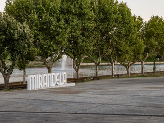Mirandela, Portugal: The riverside square with large trees and the Tua River creates a welcoming urban space, where the iconic city sign invites residents and visitors to enjoy leisure and nature.