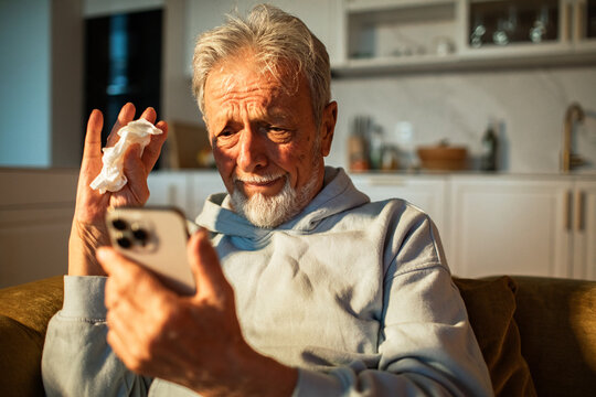Senior man emotional during video call holding tissue at home