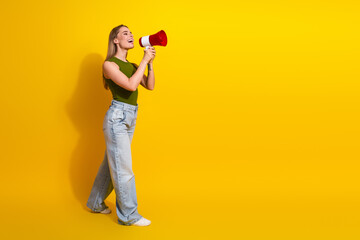 Cheerful blonde woman with megaphone on yellow background expressing happiness and showcasing casual fashion style