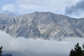 Obraz premium Majestic mountain peaks rise beneath a blue sky with light clouds. A serene and imposing landscape, ideal for projects related to nature, adventure, and tranquility.