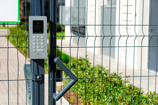 Smart intercom installed on a mesh fence. The device is equipped with a keyboard and a camera for video communication. It provides convenient access and security of the territory. - Powered by Adobe