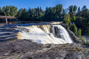 Obraz premium Kakabeka Falls, Ontario's stunning natural wonder, cascades powerfully through lush forests, offering mesmerizing scenic views and a serene escape into nature's beauty.
