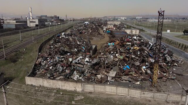 Aerial drone footage circling a scrap metal warehouse where a crane is actively moving metal across the yard