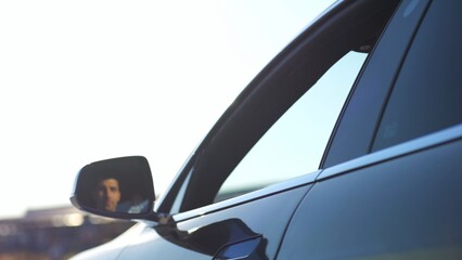 Naklejka premium Young smiling businessman in shirt leaning out of driver window at modern electric car and looking into camera. Portrait of handsome successful entrepreneur in innovative electrical vehicle. Slow mo