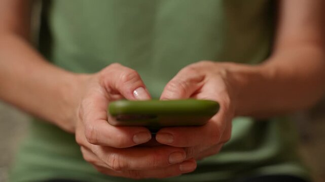 Close-up of a woman hands quickly typing on a smartphone. Fingers tapping the touchscreen, green phone case, shallow depth of field, natural indoor light, fast texting and messaging motion.