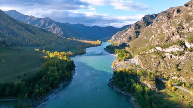 An aerial drone shot of a beautiful turquoise river winding its way through a scenic valley surrounded by majestic mountains and autumn forests