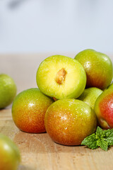 Fresh Green Plums Cut in Half Showing Juicy Yellow Flesh on Wooden Board with Water Droplets