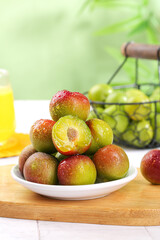 Fresh Red and Green Plums on White Plate with Cut Plum Showing Yellow Flesh