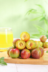 Fresh Red and Green Plums Cut in Half Showing Yellow Flesh on Wooden Board with Juice Glass