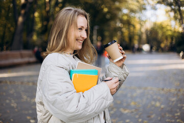 Young student woman with notebooks and coffee smiling in park.