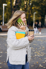 A young student woman walking in an autumn park, talking on her phone.