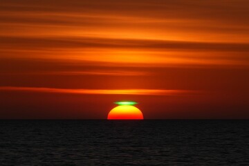 The rare and beautiful optical phenomenon of a Green Flash appearing on the top of the setting sun over the ocean horizon.