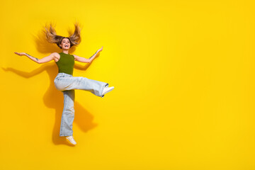 Joyful young female jumping in trendy attire on vibrant yellow background expressing energy, style,...