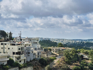 Naklejka premium Hillside homes overlook a wide expanse of forest and distant neighborhoods beneath a sky scattered with soft clouds