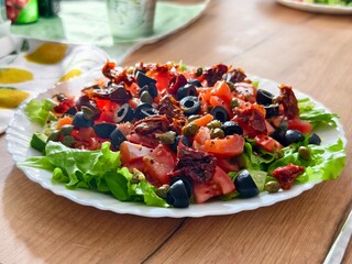 Fresh salad with tomatoes olives capers and sun dried tomatoes served on a white plate on wooden table