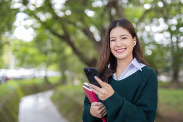 Asian female student in warm clothes using phone to chat with friends and ready for video call while in university.