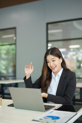  A beautiful businesswoman in a suit is looking at a computer screen while talking on her mobile phone. She is sitting in an office and using modern technology.