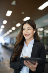 Asian businesswoman standing in front of modern business building and using tablet to work.