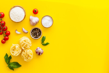 Flat lay of ingredients for cooking Italian pasta - uncooked fettuccine with tomatoes and basil leaves - on a yellow background, top view