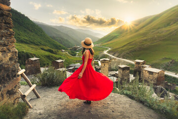 Woman in red dress looking at medieval towers of Ushguli Georgia during sunset with mountains and...