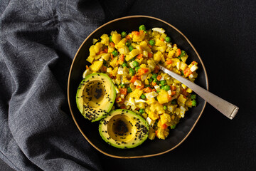 A colorful salad combines boiled egg, tender chicken breast, diced potatoes, vibrant carrots, and fresh green peas, topped with creamy avocado and sesame seeds, all drizzled with olive oil