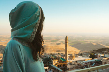Smiling woman traveler in abaya standing above Mardin Turkey with panoramic view of Mesopotamian...