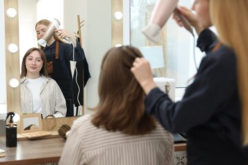 Hairstylist blow drying client's hair in salon, closeup