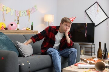 Man suffering from hangover on sofa in messy room after party