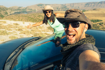 Happy young caucasian couple taking selfie while sitting in rented vehicle black car having road trip Europe. Outdoor lifestyle activity on road trip vacation concept. Excited happy couple enjoy ride
