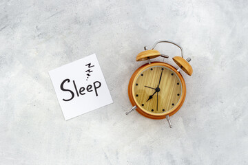 Retro alarm clock with paper card with hand drawing of Sleep word, top view. Time management...