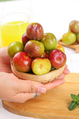 Fresh Red and Green Plums in Wooden Basket Held by Hands with Cut Pieces Showing Yellow Flesh