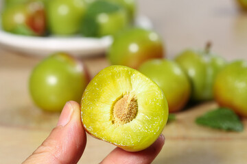 Fresh Green Plum Cut in Half Showing Juicy Pulp and Pit in Hand