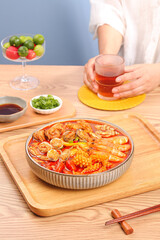Spicy seafood hotpot with fresh shrimp and clams in red broth served with tea on wooden table