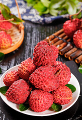 Fresh Red Lychee Fruits on White Plate with Cinnamon Sticks and Tropical Fruit Display on Rustic Wooden Background